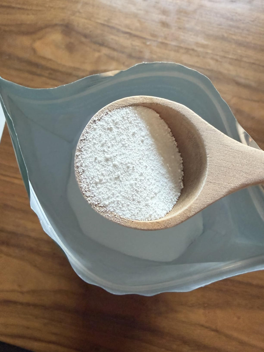 Primer plano del detergente y la cuchara de madera sobre la bolsa abierta.